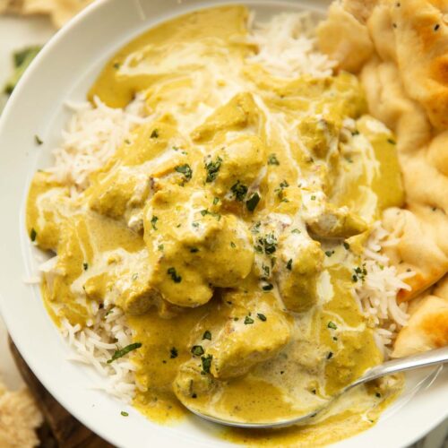close up shot of chicken korma in large white dish on rice with naan bread