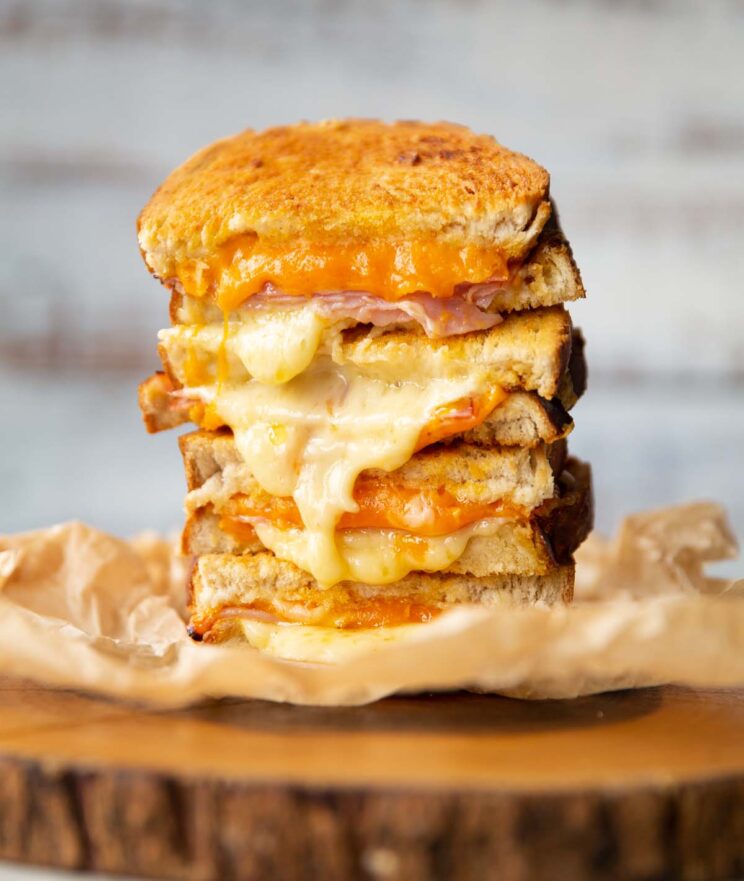 4 toastie halves stacked on each other with cheese spilling out on wooden board