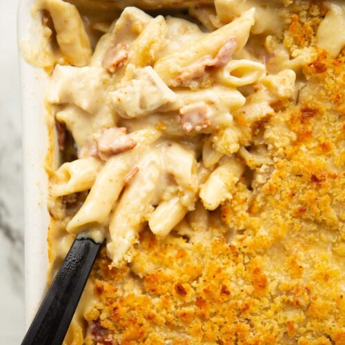 overhead close up shot of chicken bacon pasta bake with black serving spoon digging in
