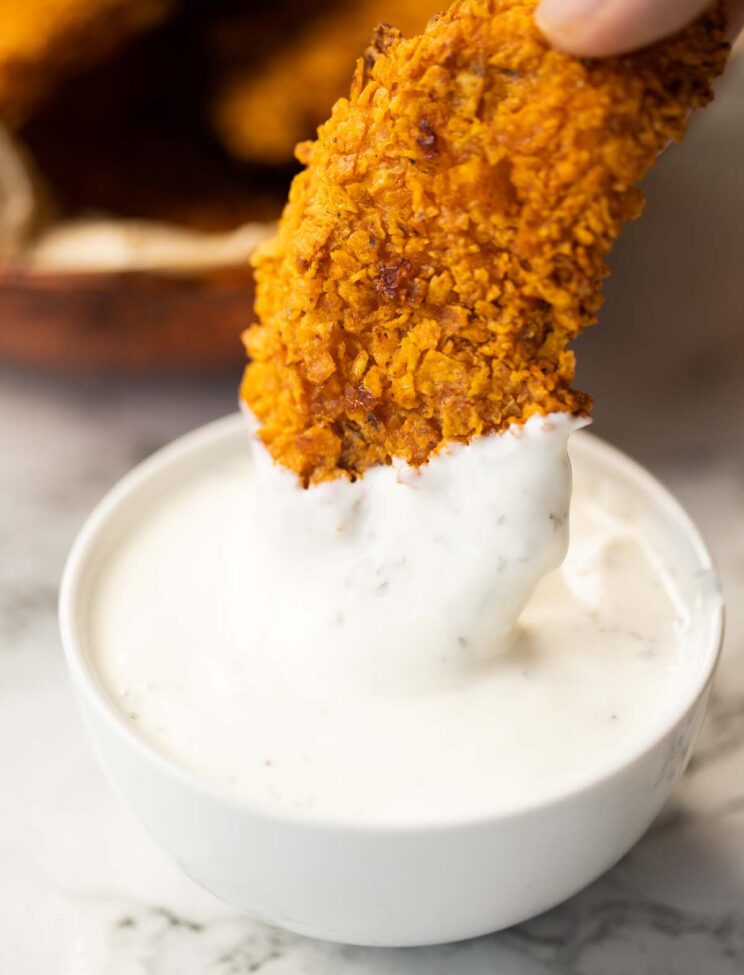 close up shot of doritos crusted chicken tender dunking into small pot of ranch