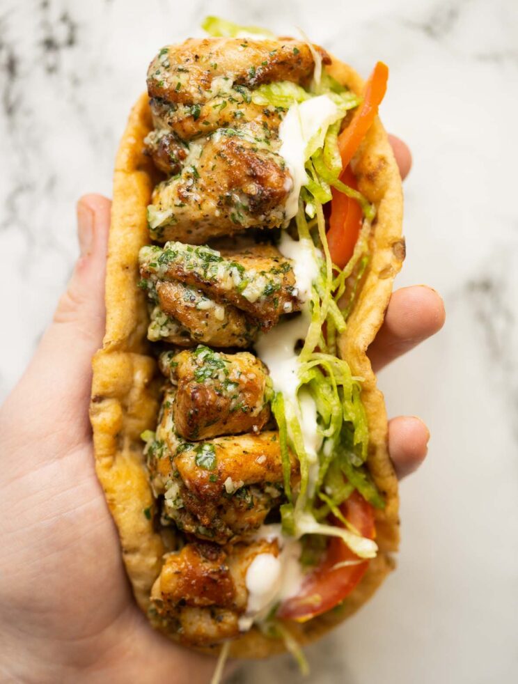 close up overhead shot of hand holding garlic butter chicken skewers in flatbread